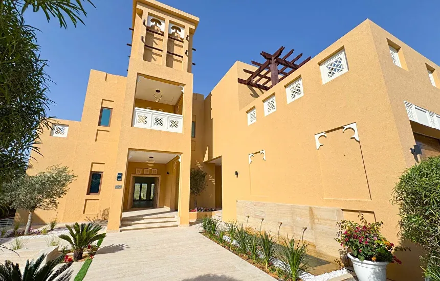 Sand-coloured Dubai villa with a decorative wind tower, carved screens and a pergola on a sunny day