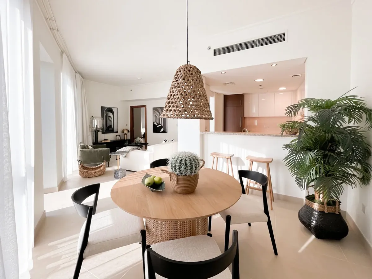 Open-plan Dubai apartment with a ceiling air-conditioning grille, woven pendant light and a round dining table