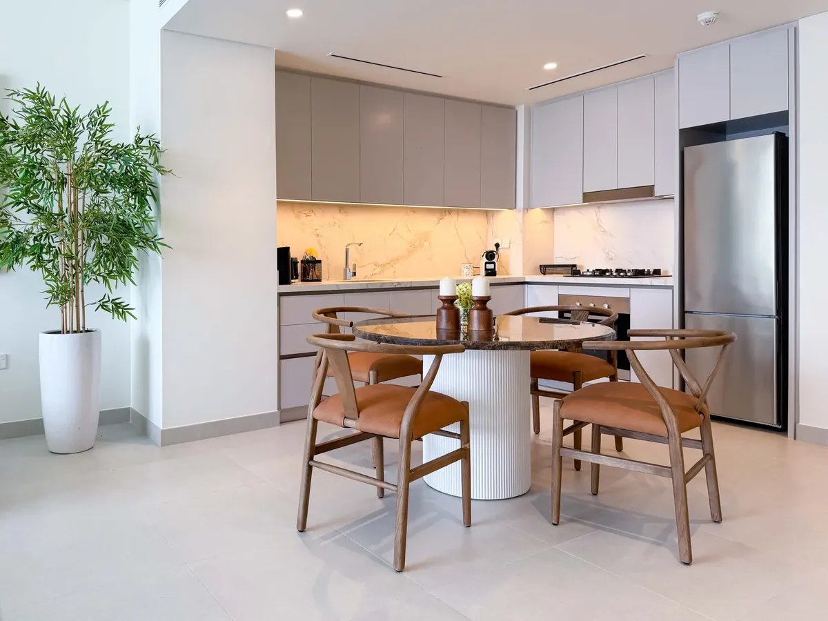 Compact apartment kitchen with light cabinets, marble splashback and a round dining table