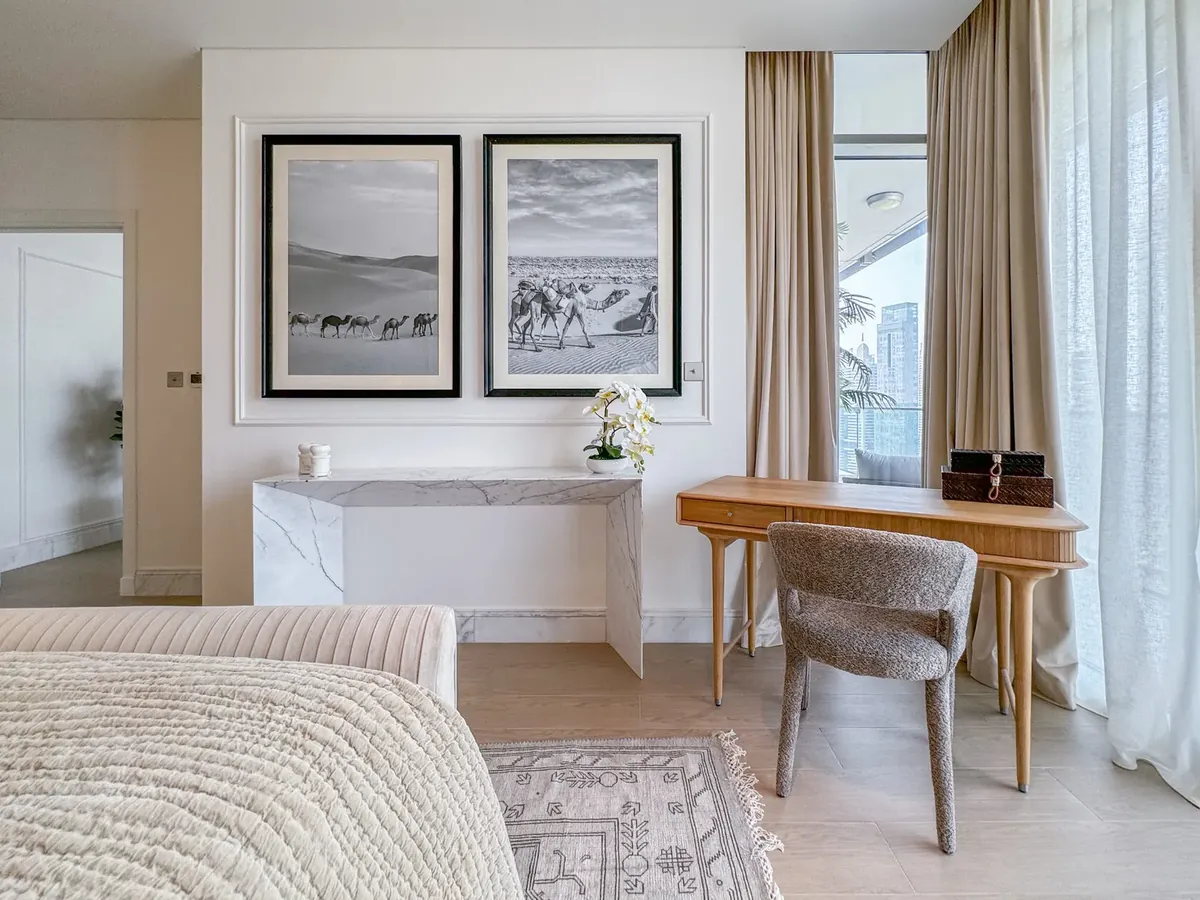 Timber desk and stone-topped console with framed black-and-white desert photographs in a bedroom
