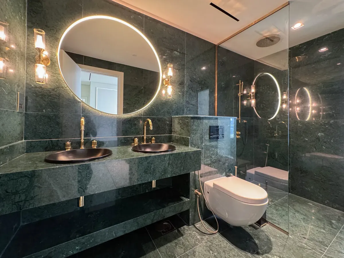 Renovated Dubai bathroom with green marble vanity, round backlit mirror and frameless glass shower