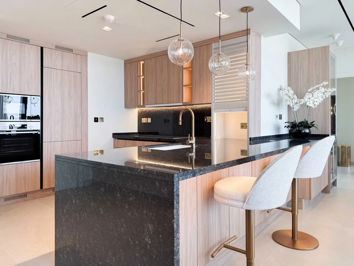 Modern Dubai kitchen with dark stone island worktop, timber-veneer cabinets and pendant lights