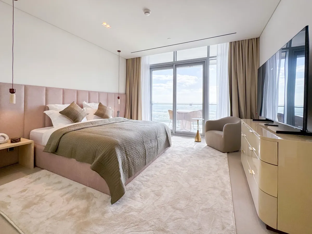 Bedroom with a pink upholstered wall panel behind the bed, floor-to-ceiling windows and a wide cream rug