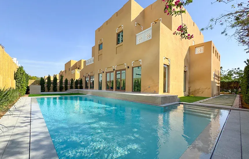 Villa swimming pool with stone coping and lawn beside a sand-coloured Dubai villa in afternoon sun