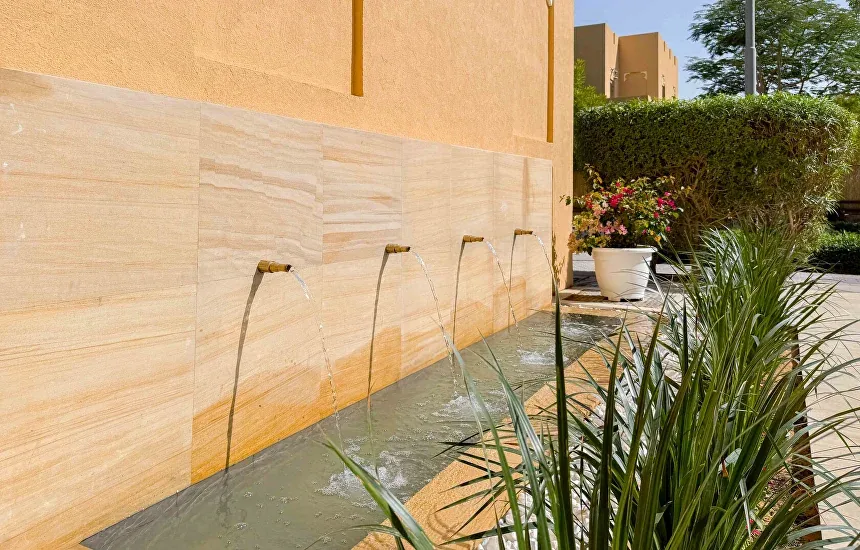 Stone feature wall with four water spouts feeding a shallow pool, with planting in the foreground